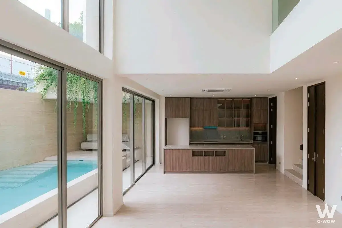 Open-plan living kitchen with double-height ceilings and pool view in Ban Chan Condominium