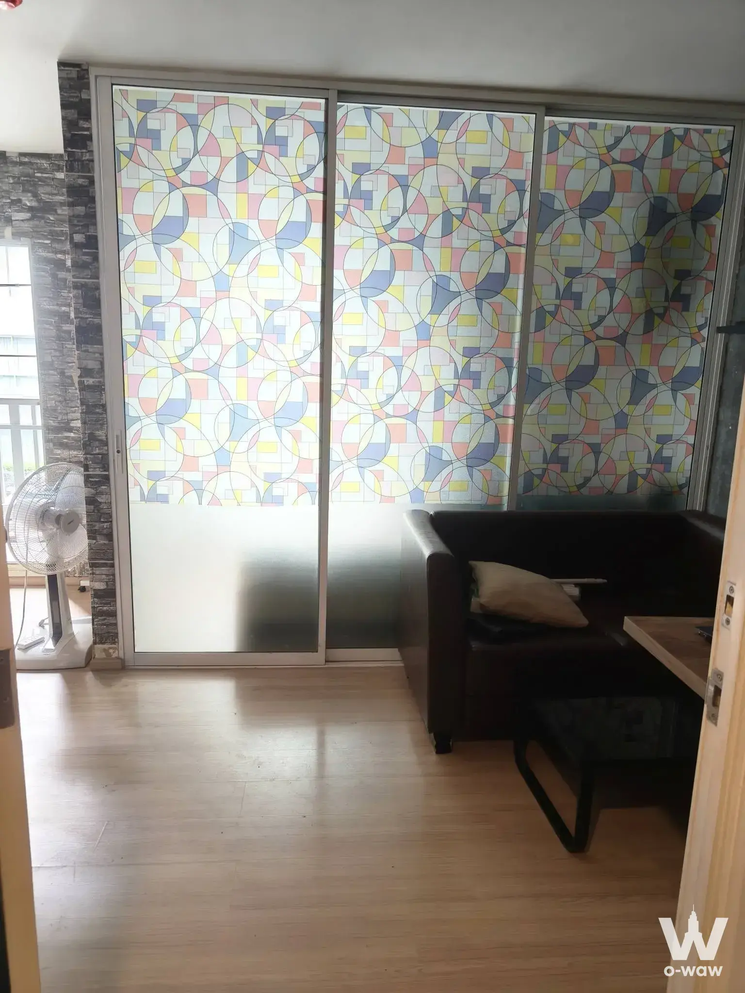 Modern living room in 1-bed Plum Condo Ladprao 101 with wood floors, leather sofa, and pastel geometric roller blinds