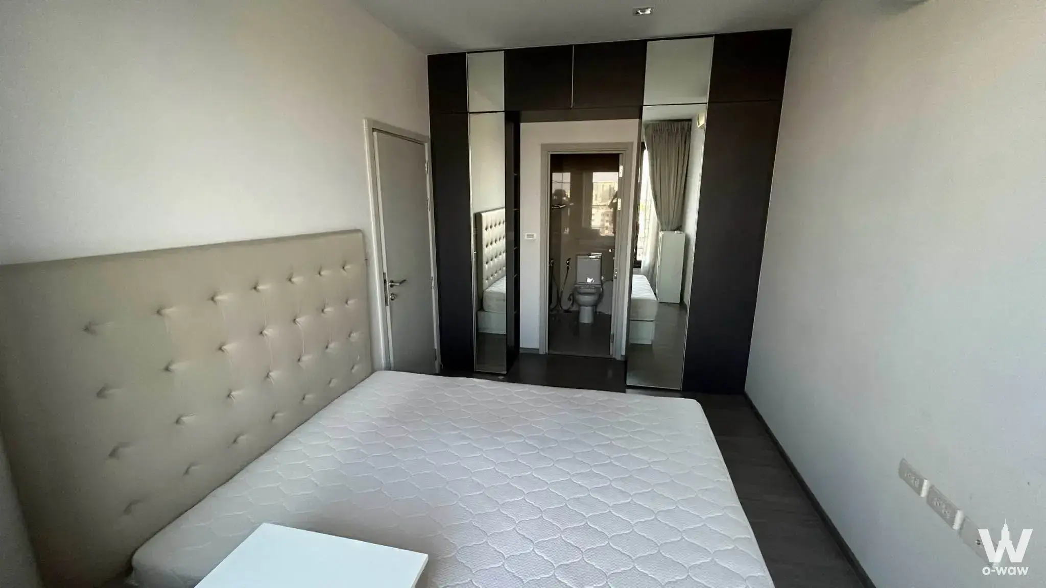 Nye by Sansiri 1-bed condo bedroom has a white queen mattress, beige leather headboard and mirrored wardrobe