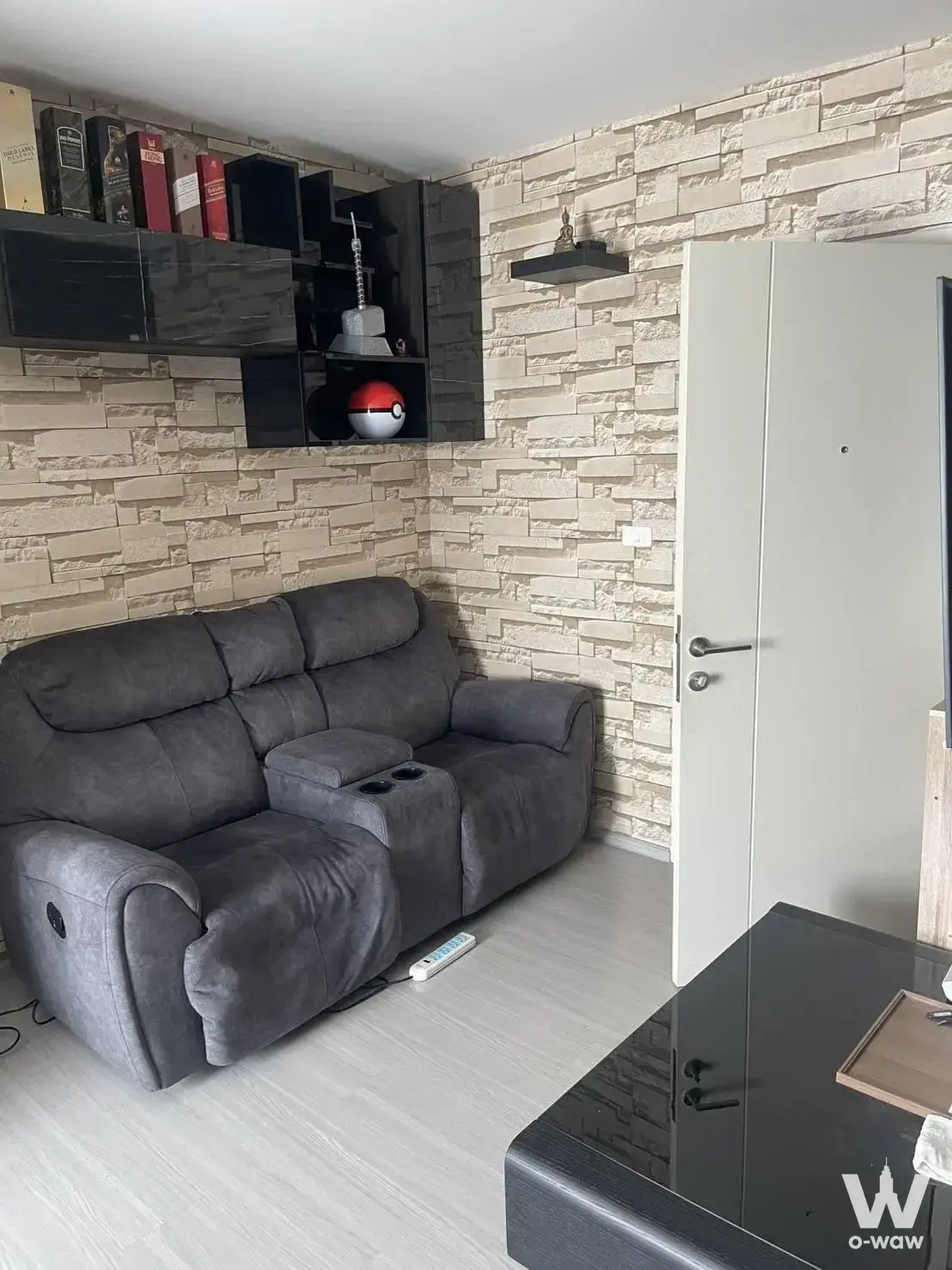 Casual living room in a Sathorn condo with dark grey recliner sofa and textured stacked-stone wall paneling