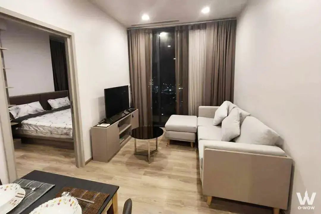 Furnished Oka Haus condo living space featuring a beige sectional sofa and city night view through glass doors