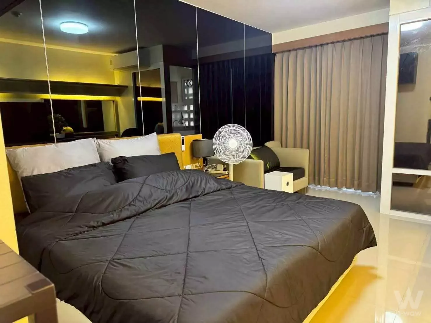 Modern bedroom in 1-bed Garden House rental with yellow headboard, mirrored wardrobe, and glossy tile floors