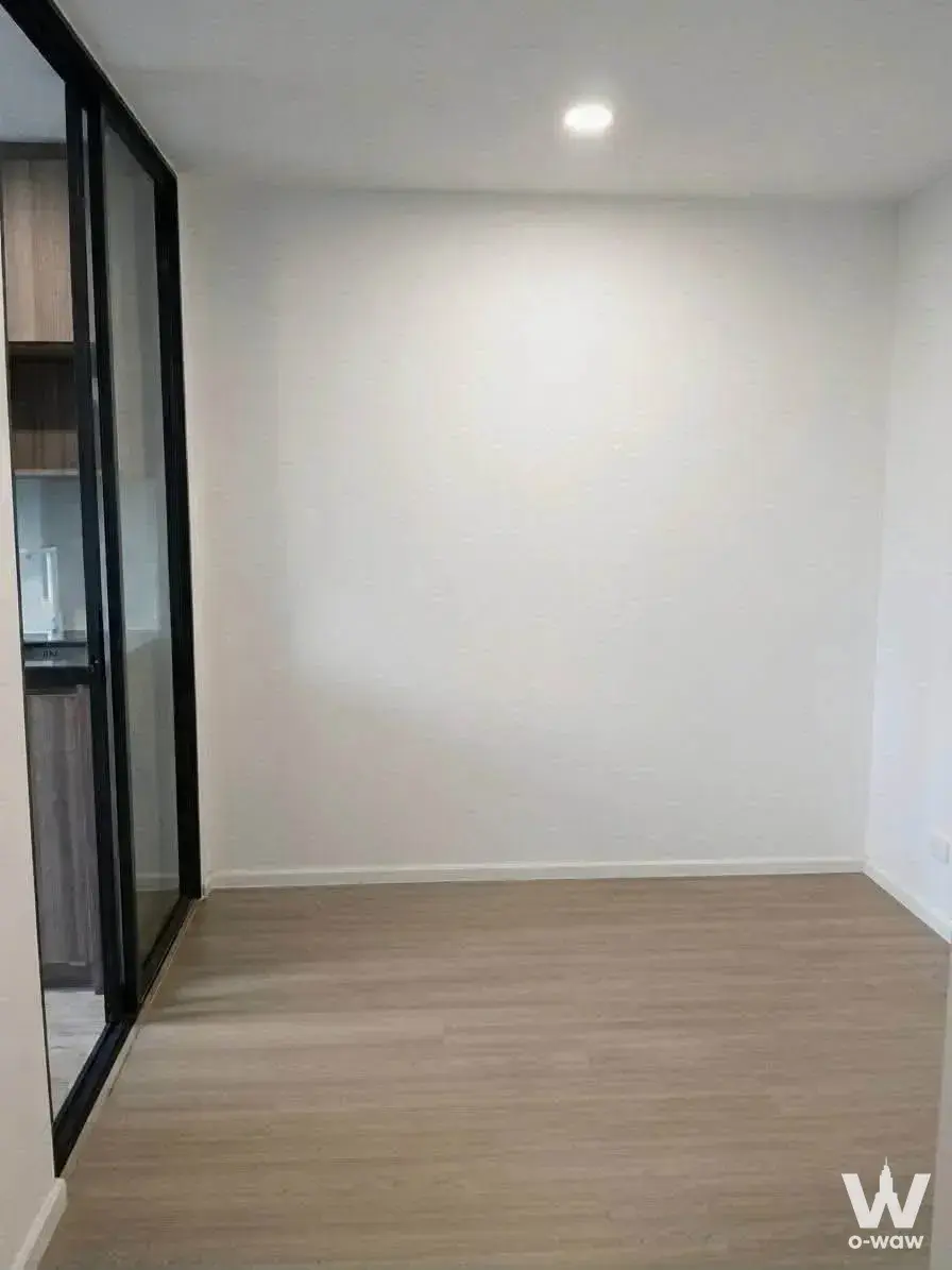 Empty room in Cerocco Bangna 36 condo with light wood floors and glass door to kitchenette