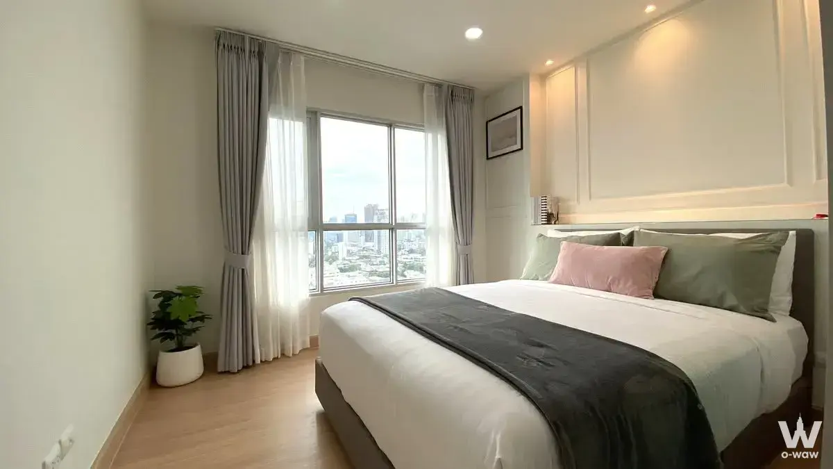 Queen bed in 1-bed Aspire Rama 4 condo rental with city view, light wood floors, and sage green accents