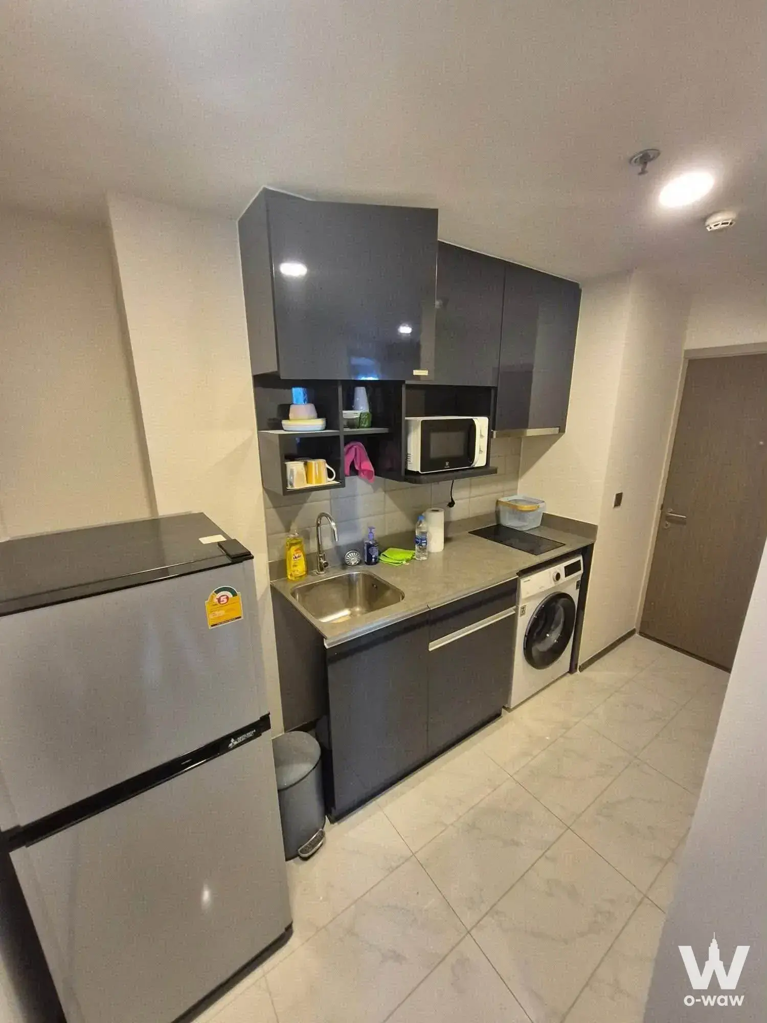 Compact kitchenette in Ideo Q Siam-Ratchathewi condo with dark grey cabinets and stainless steel sink
