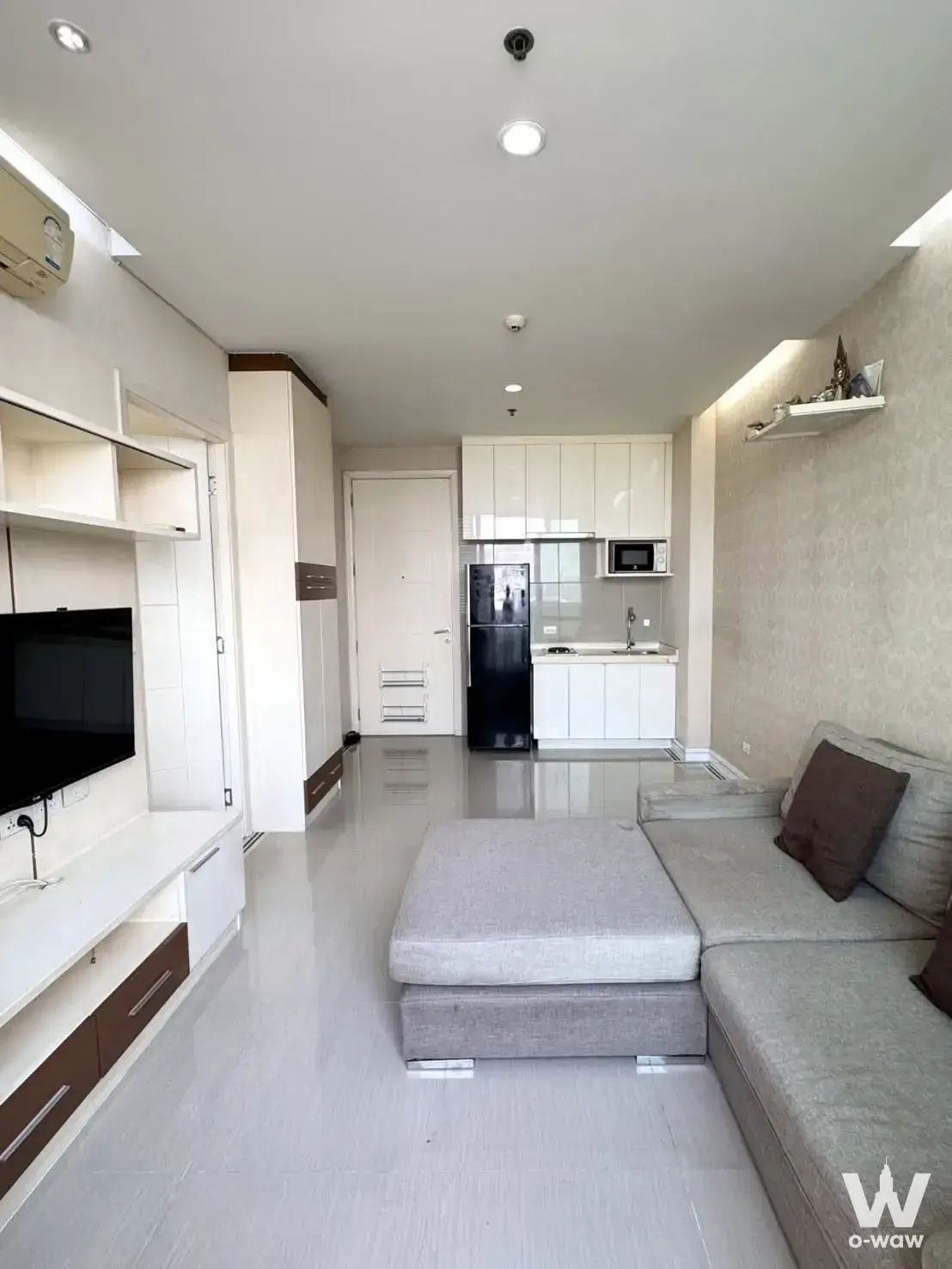 Modern living room in 1-bed for sale at TC Green Rama 9 with grey sofa and glossy white tiles