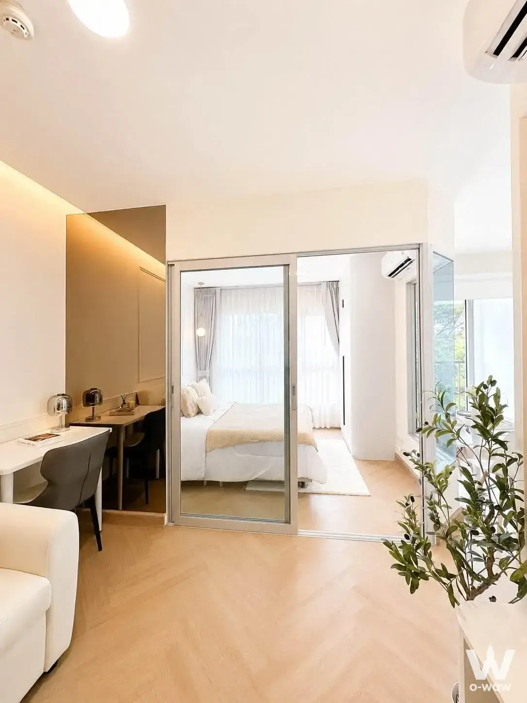 Open-plan bedroom in Aspire Rama 4 condo with herringbone oak floors and gold-toned mirror