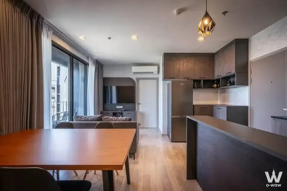 Modern condo living and dining area with wood floors, grey sofa, kitchen counter, and floor-to-ceiling windows overlooking