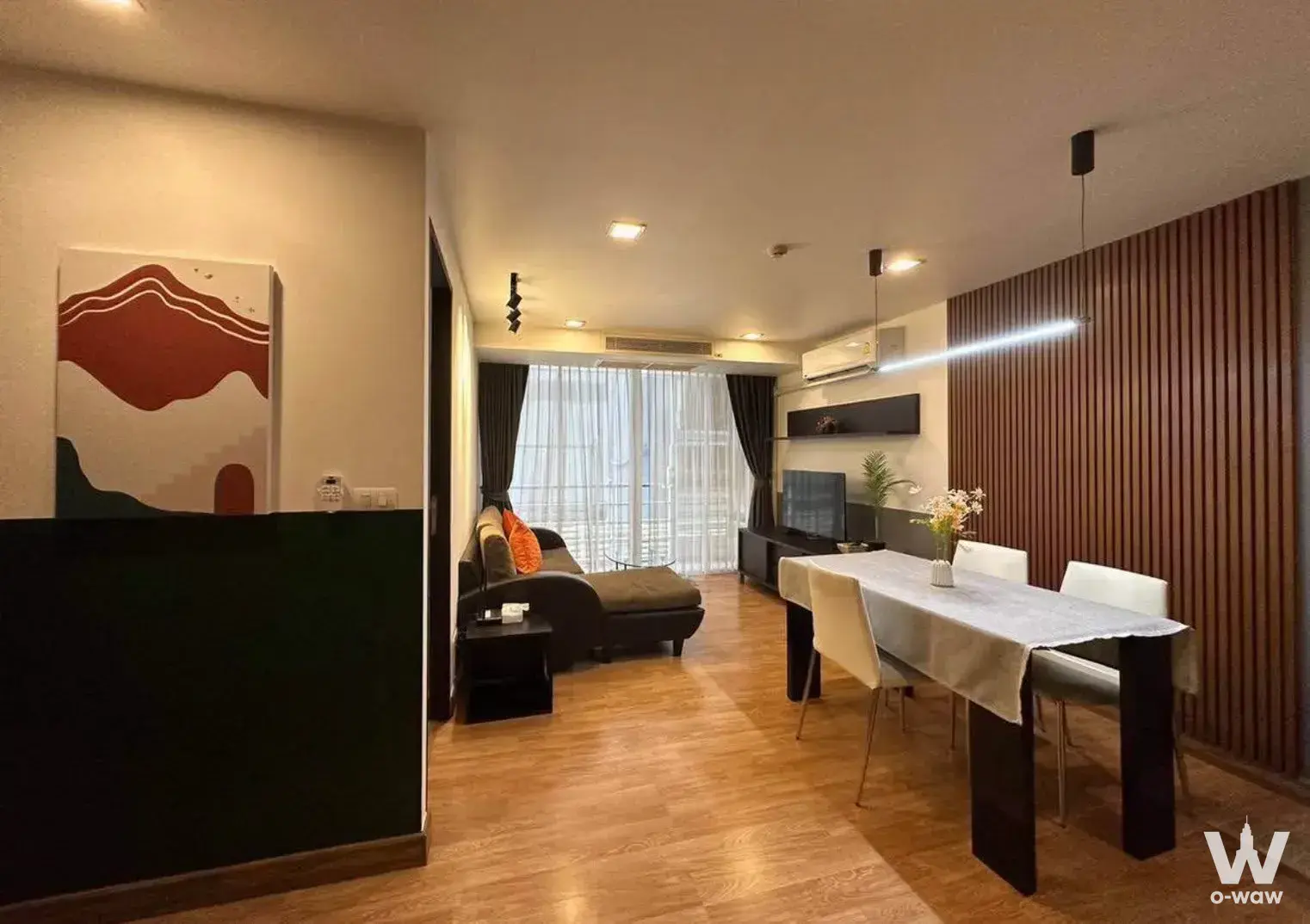 Living area with dark brown leather chaise lounge, vertical wood slat accent wall, and city view