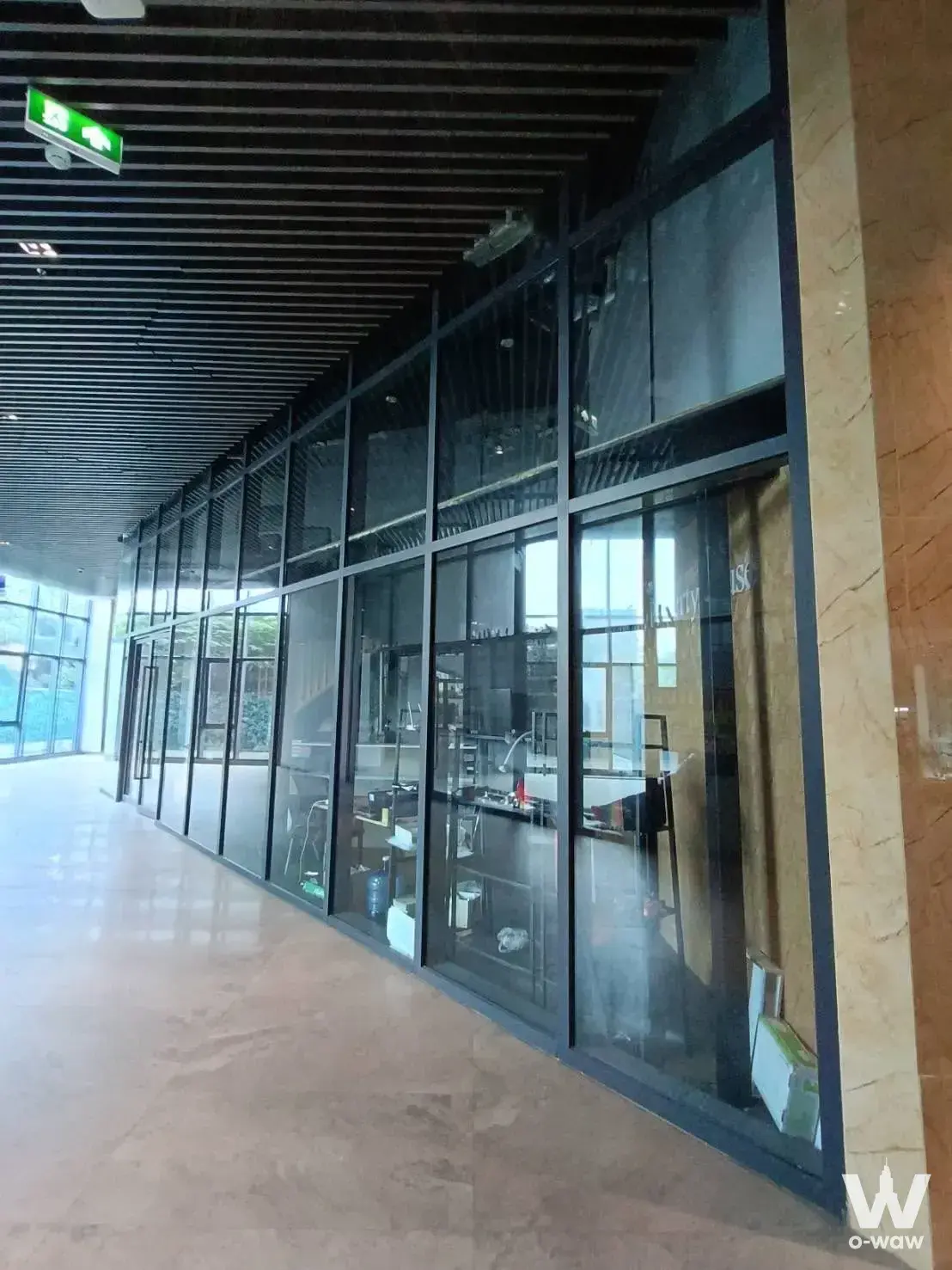 Modern commercial corridor at Artisan Ratchada with polished marble floors, black-framed glass walls, and natural light from