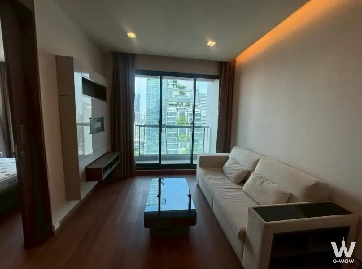 Living room with glass balcony doors and skyline view in a 1-bed condo for rent at The Address Sathon