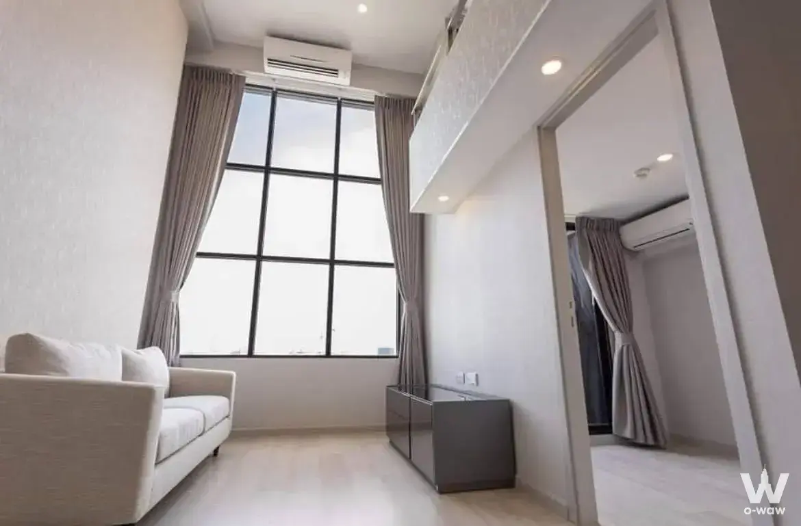 Living room in a Sathon condo featuring double-height ceilings and floor-to-ceiling windows with black grid frames
