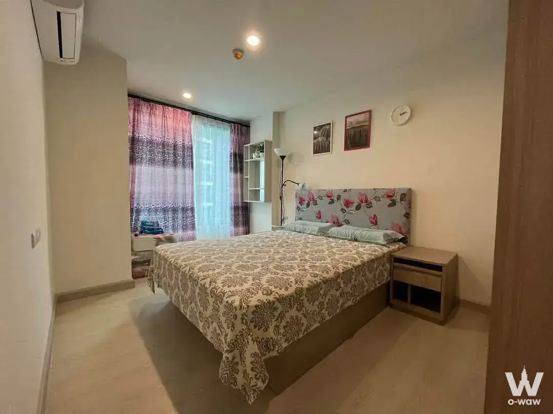 Queen bed with floral headboard and green pillows in a 1-bed rental at The Niche Mono Sukhumvit 50