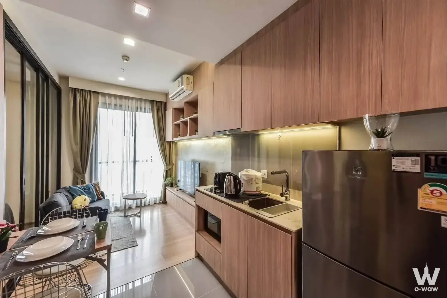 Fully furnished open-plan studio with light wood floors and modern kitchen amenities at M Jatujak