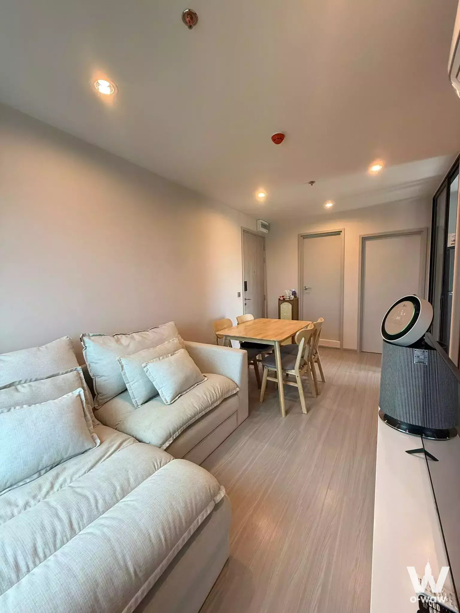 Open-plan living and dining area in 2-bed Aspire Erawan Prime condo featuring light wood floors and L-shaped sofa