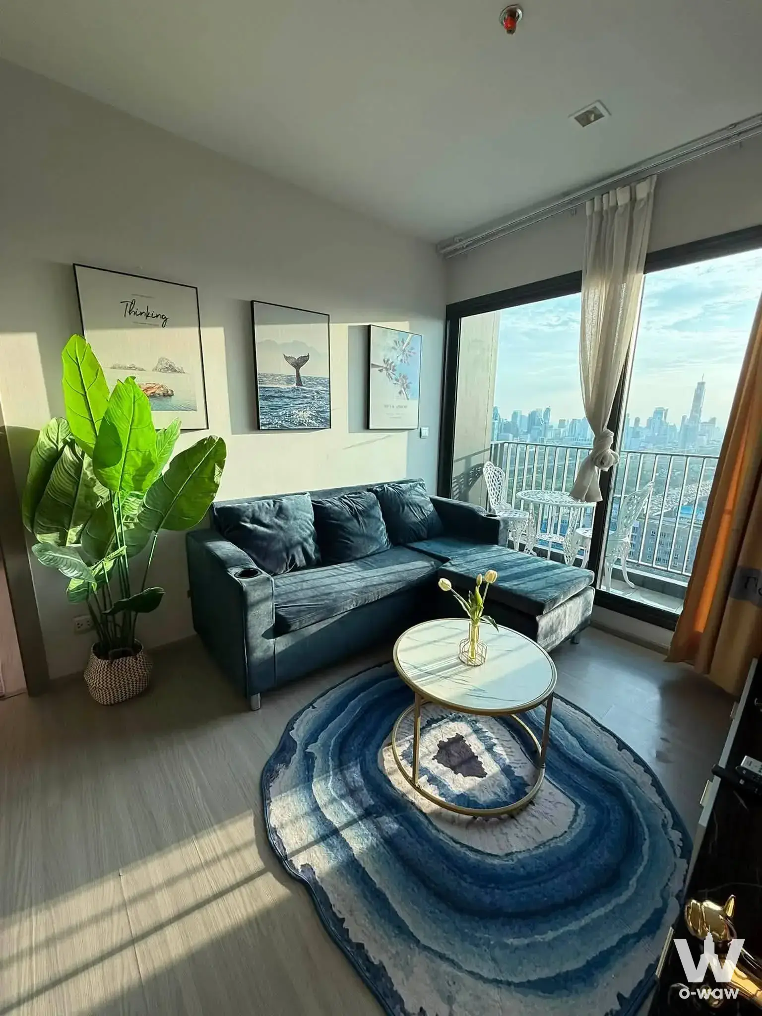 Modern condo living room with teal sectional sofa and marble coffee table overlooking Bangkok city skyline