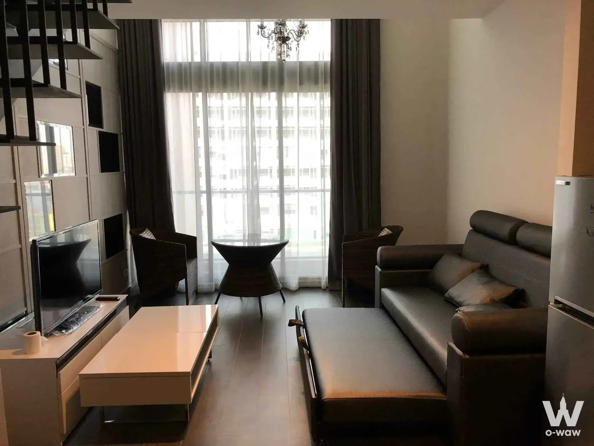 Modern living room in 1-bed Ekkamai rental with grey sofa, open staircase, and city views