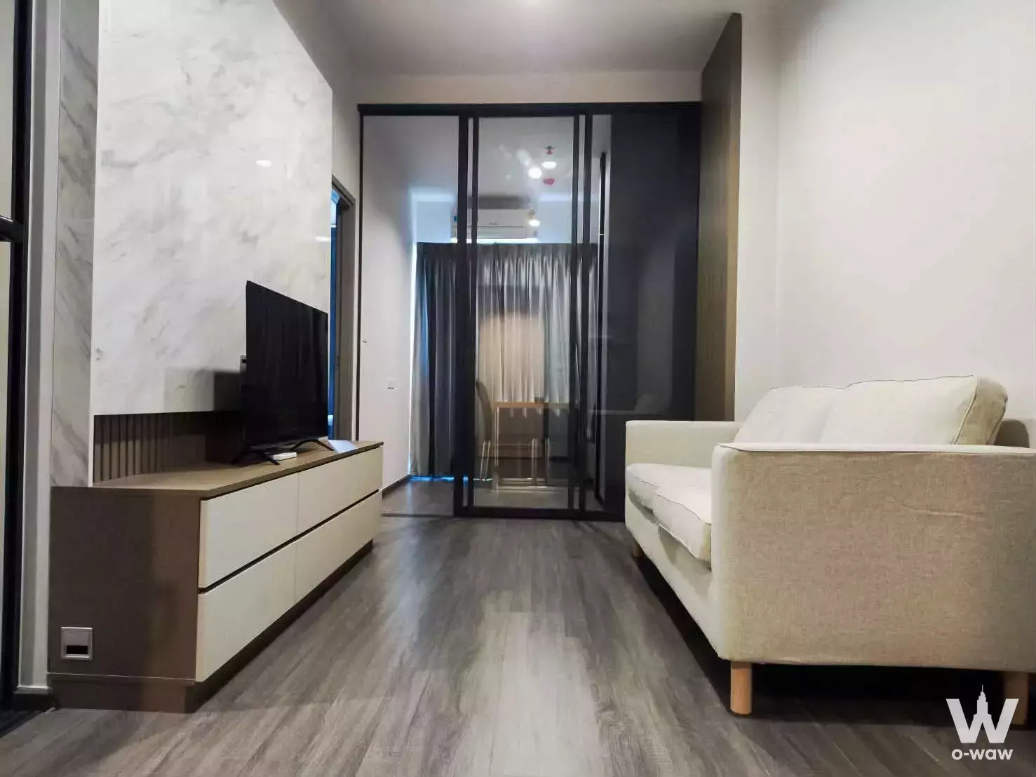 Modern 1-bed condo living room in IdeO Sukhumvit Rama 4 with marble accent wall, beige sofa, and glass sliding doors