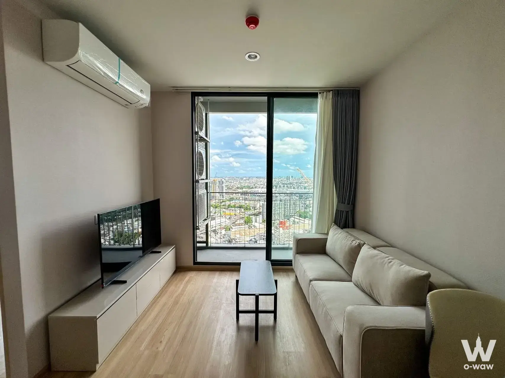 Bright living room with beige sofa and city view at Skyrise Avenue Sukhumvit 64