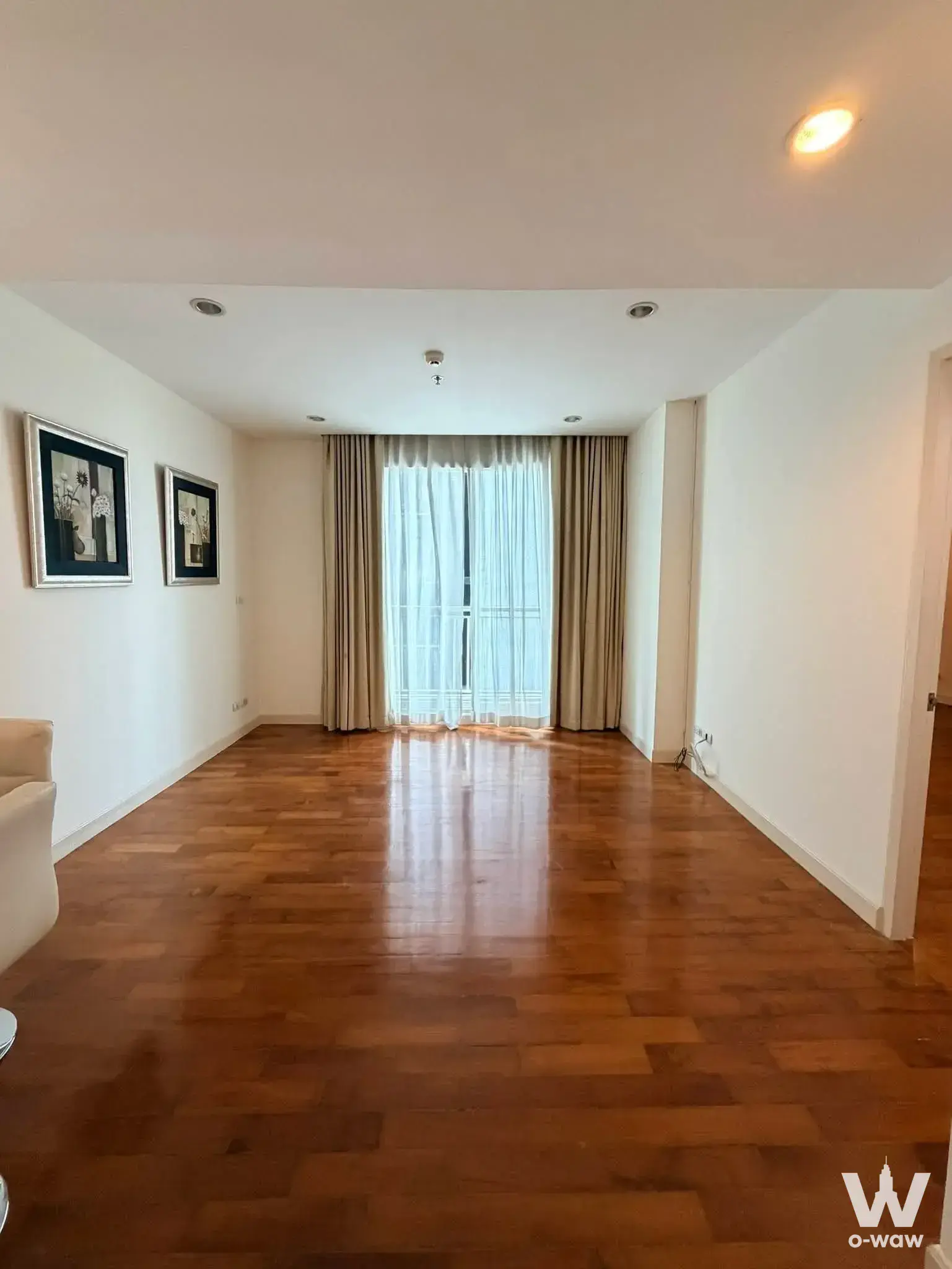 Empty living room with polished wood floors and balcony access in a Baan Siri Thirty One condo for sale