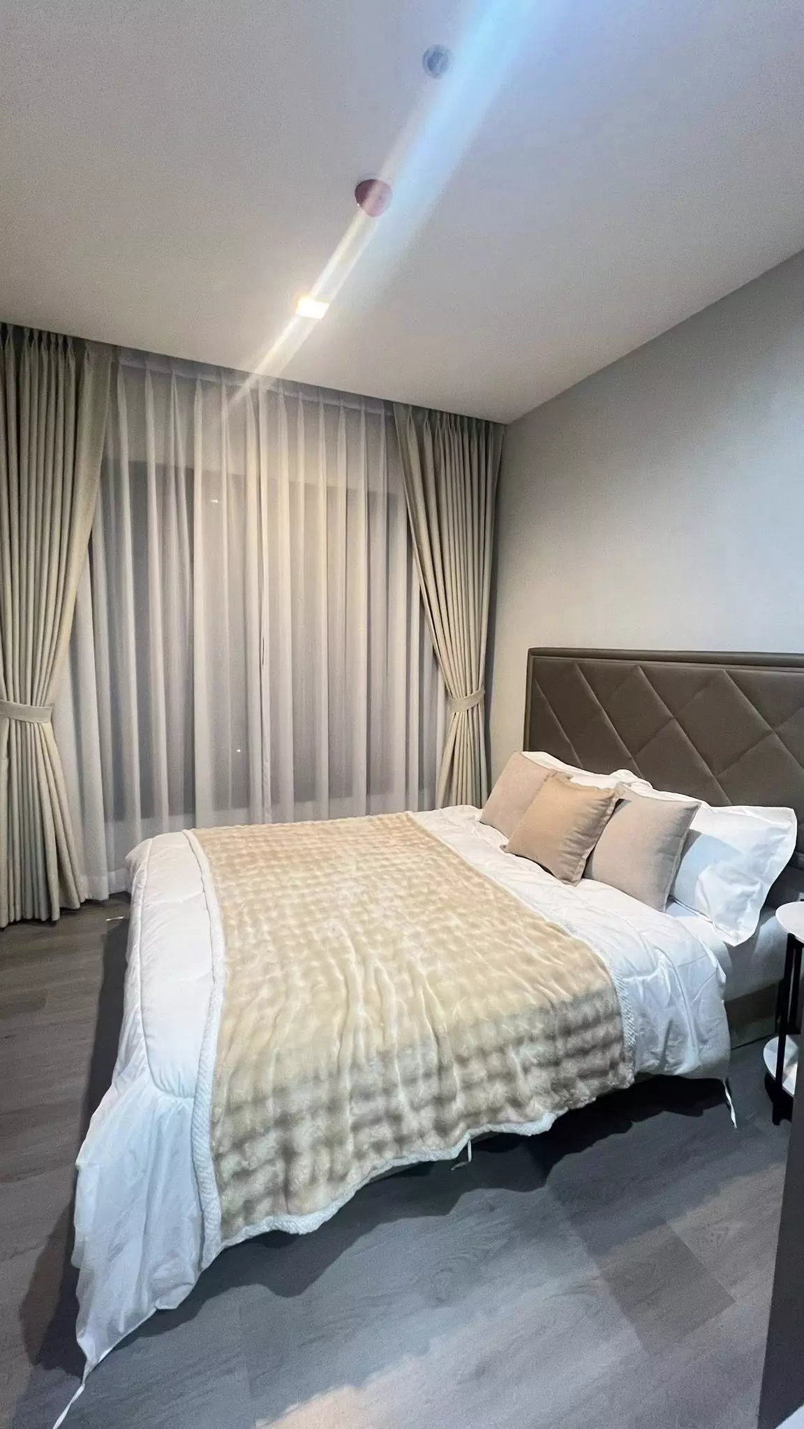 Modern bedroom in 2-bed Politan Rive condo with taupe tufted headboard and large window