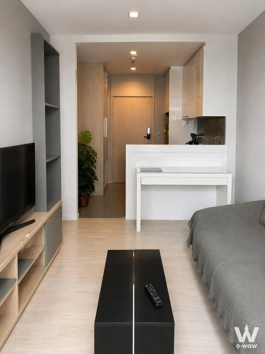 Open-plan studio in M Thonglor 10 with grey sofa, media console, and built-in shelving unit
