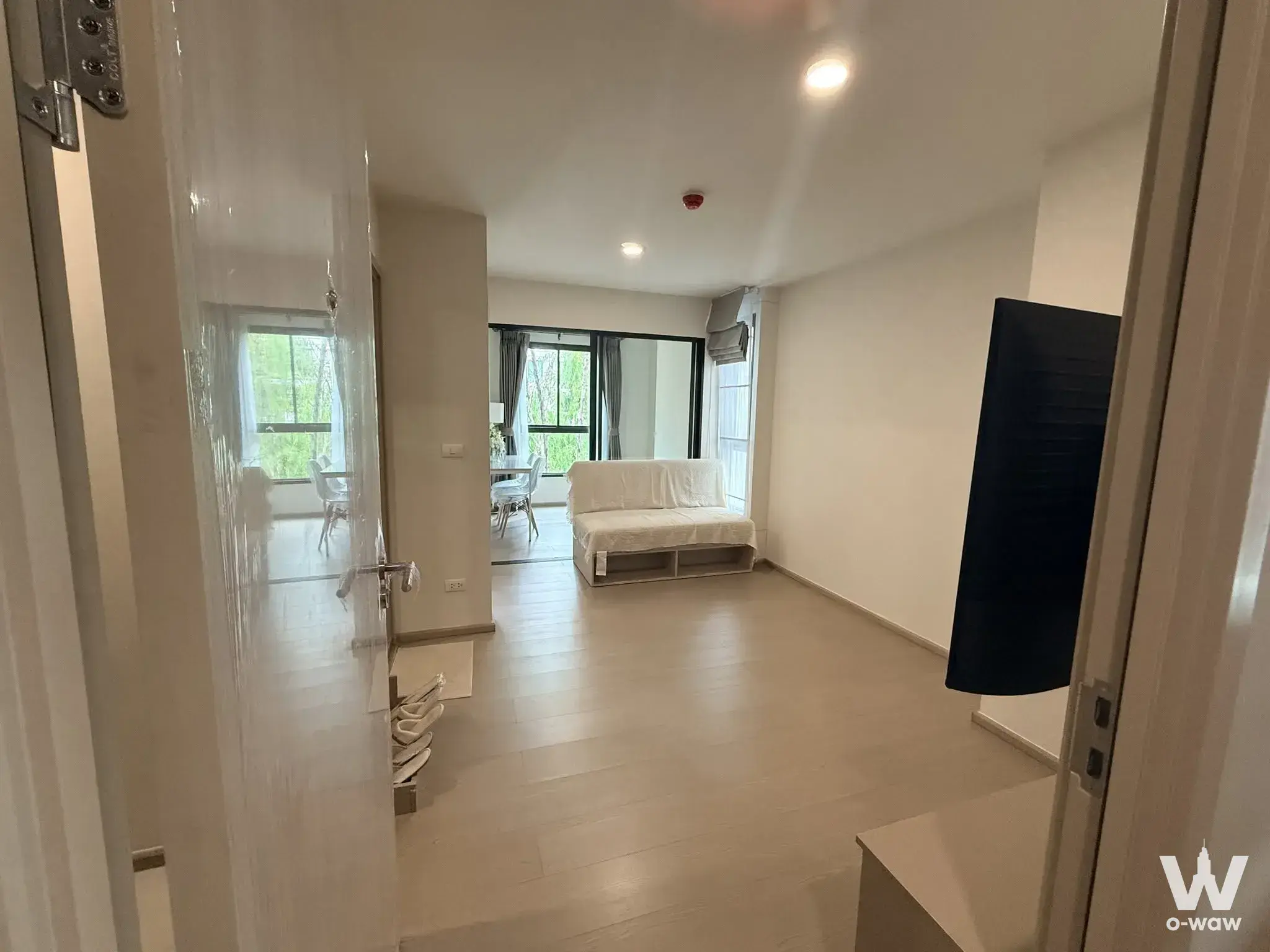 Minimalist entryway with light wood floors and sliding glass doors to a tree view in a GOOD DAY Sukhumvit 93 condo