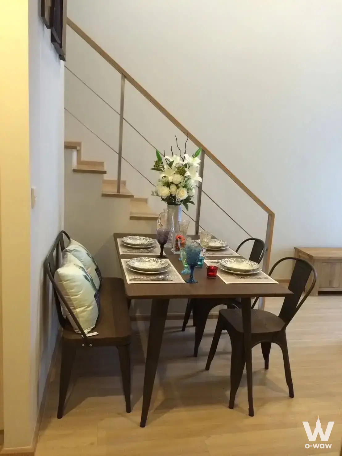 Compact dining nook under staircase with wooden table, bench seating, and modern decor in 2-bed Maestro 12 Ratchathewi condo