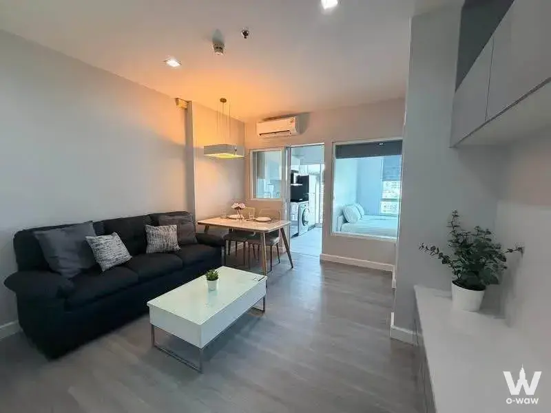 Modern 1-bed condo for rent in The Room Ratchada-Ladprao with open-plan living area, charcoal sofa, and city view from