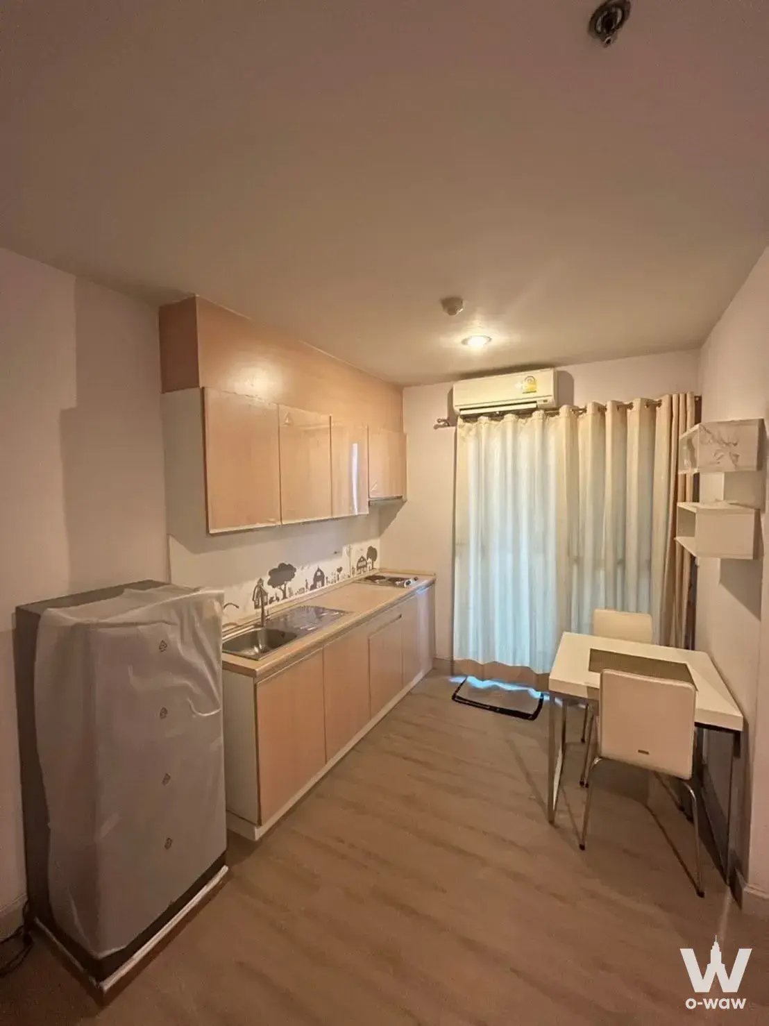 The Parkland Srinakarin Lakeside studio kitchenette with light wood cabinets, skyline backsplash, and dining area