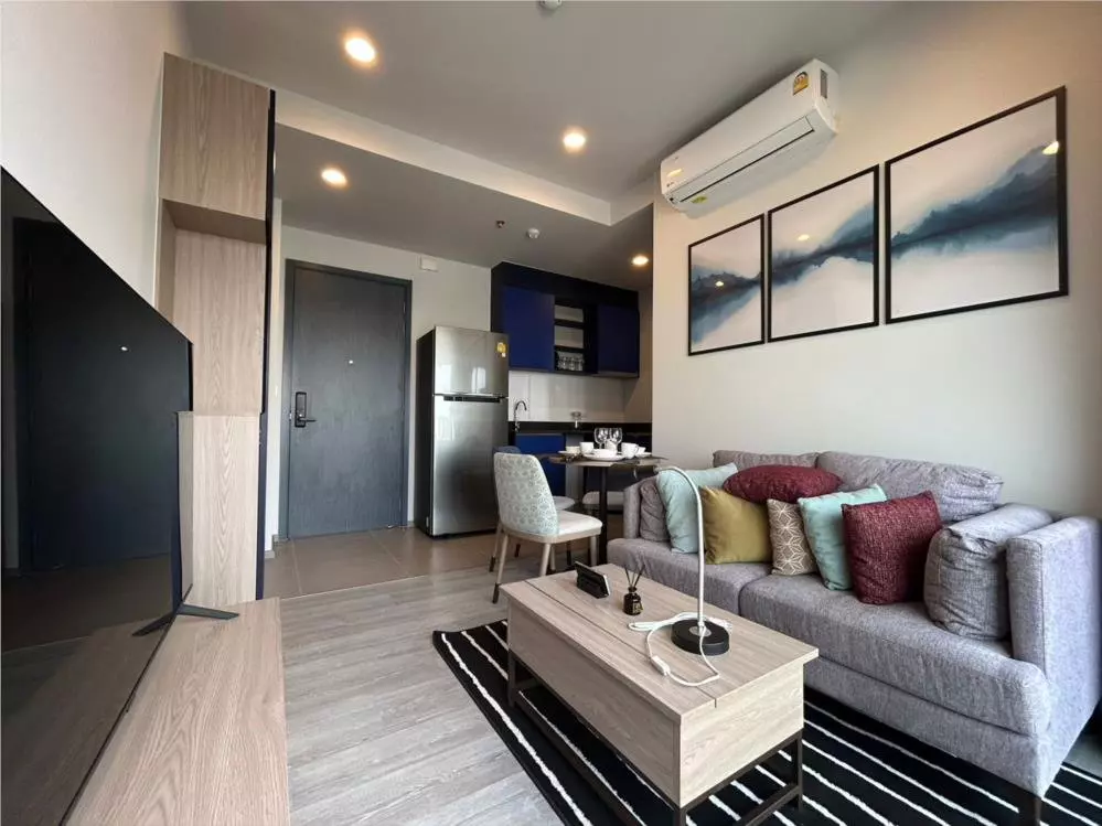 Modern living room with grey sofa, striped rug, and open kitchenette in 2-bed condo for rent at XT Ekkamai