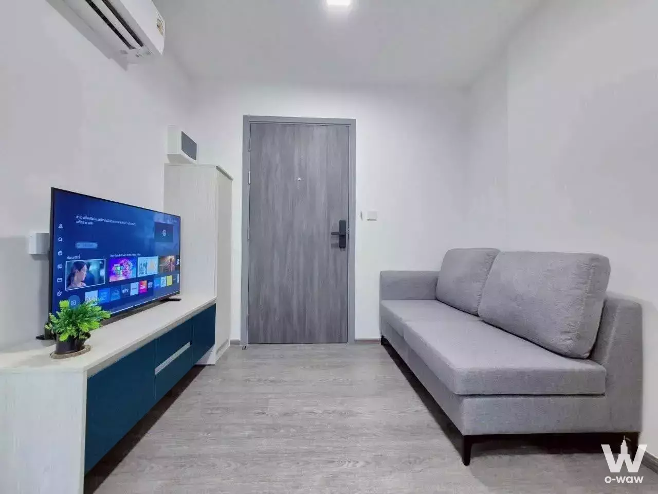 Modern living room in 1-bed Kave Wonderland rental with grey sofa, teal media console, and smart lock door