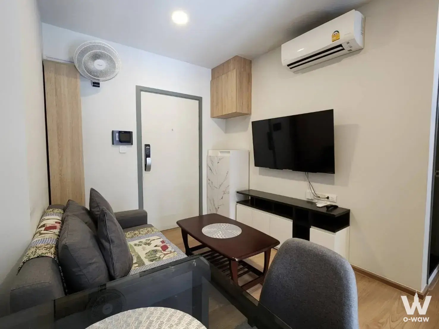 Compact living room with grey sofa and dining table in a 1-bed condo for sale in Chewathai Pinklao