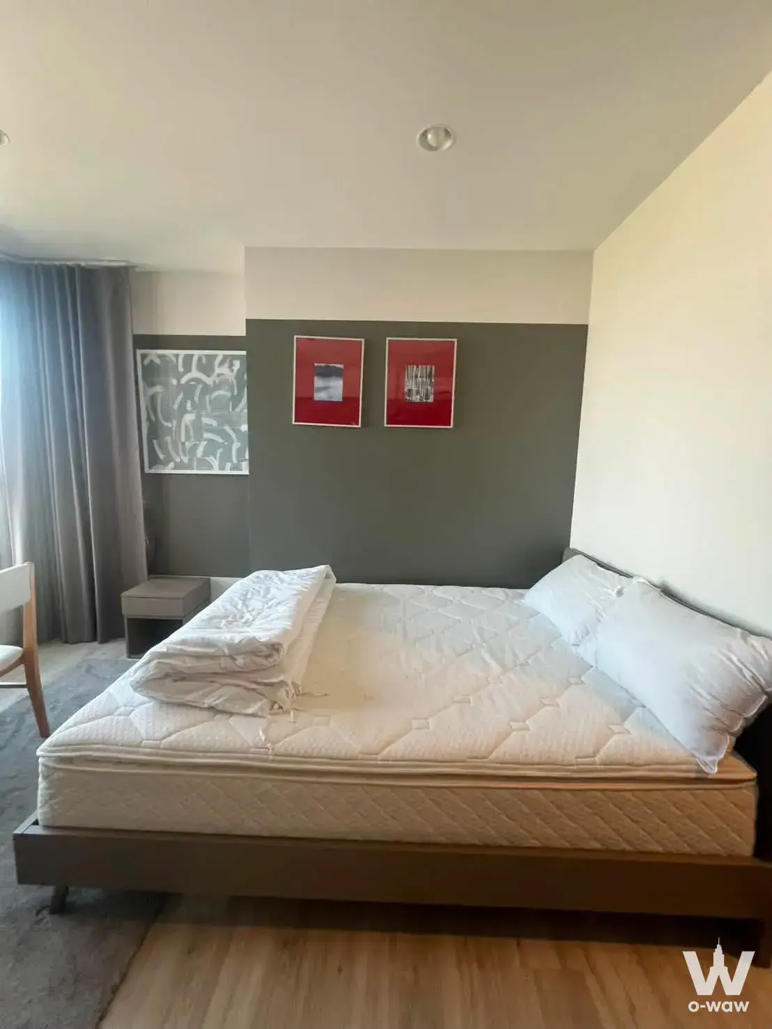 Modern bedroom in 1-bed condo for rent at XT Huai Khwang featuring light wood floors, grey accent wall, and abstract art