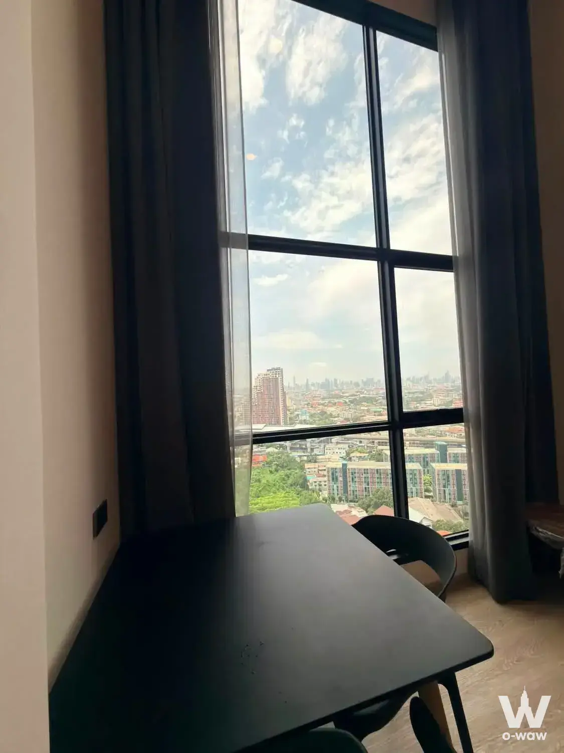 Modern condo workspace with black desk and chair facing a floor-to-ceiling window with city views