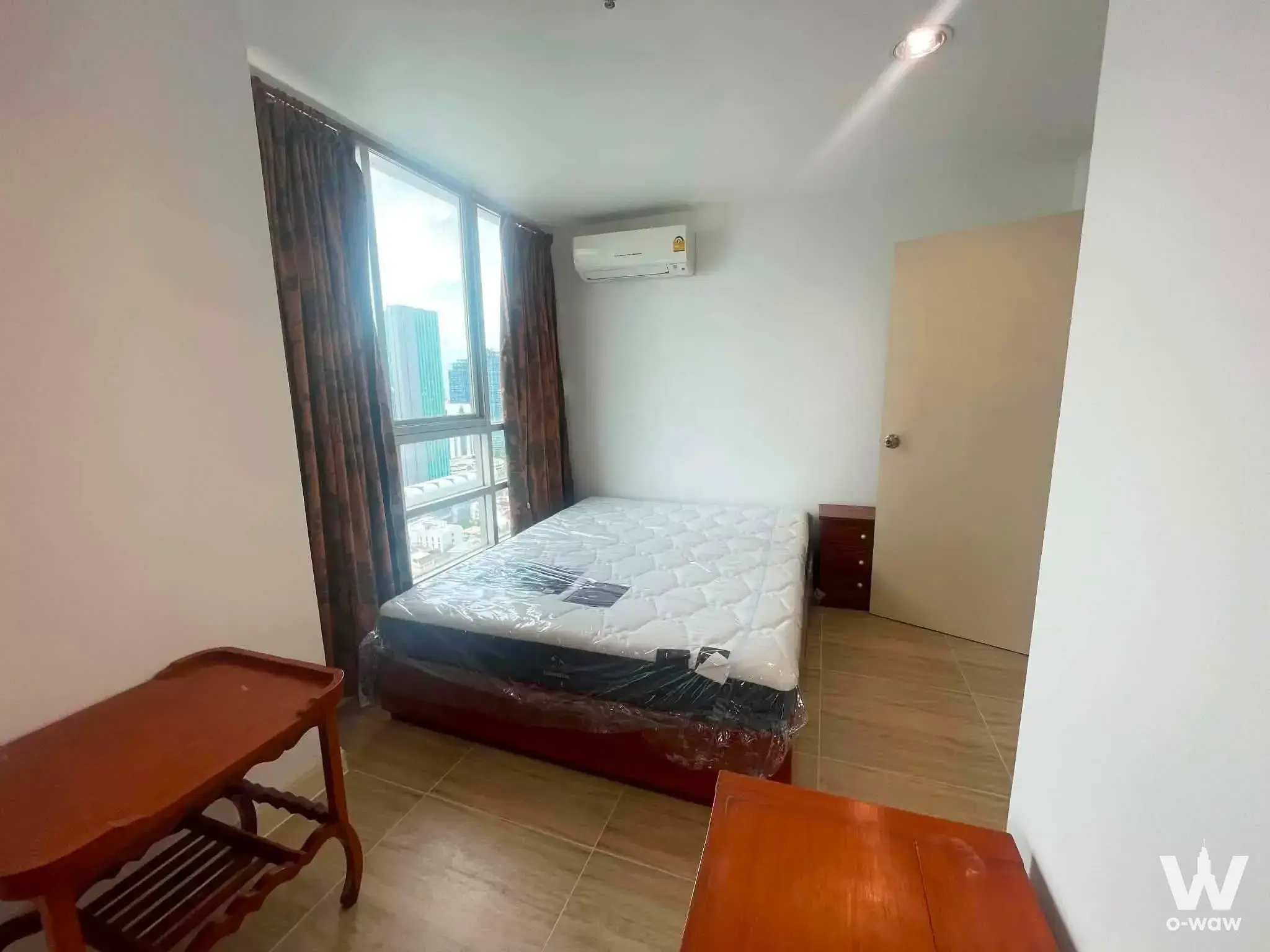 Bedroom in 2-bed Baan Pathumwan condo with city view from floor-to-ceiling windows and wooden furniture