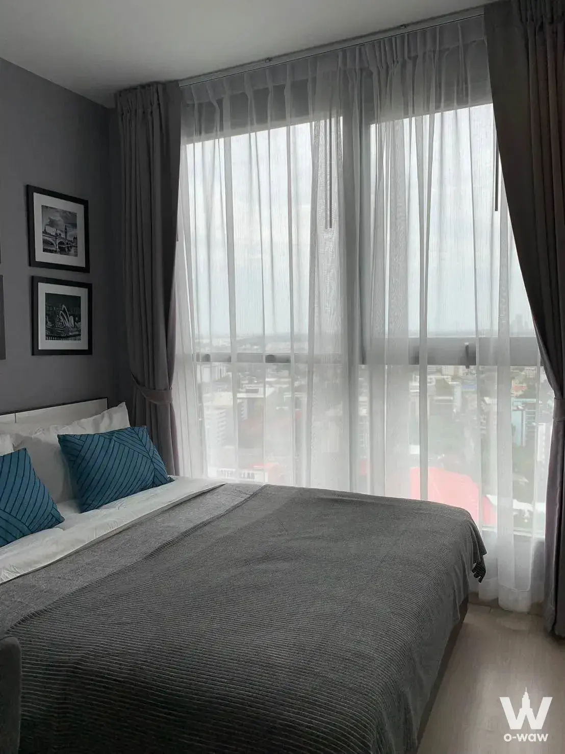 Bedroom in Ideo Mobi Sukhumvit 81 condo with grey bedding, teal accents, and high-floor skyline views