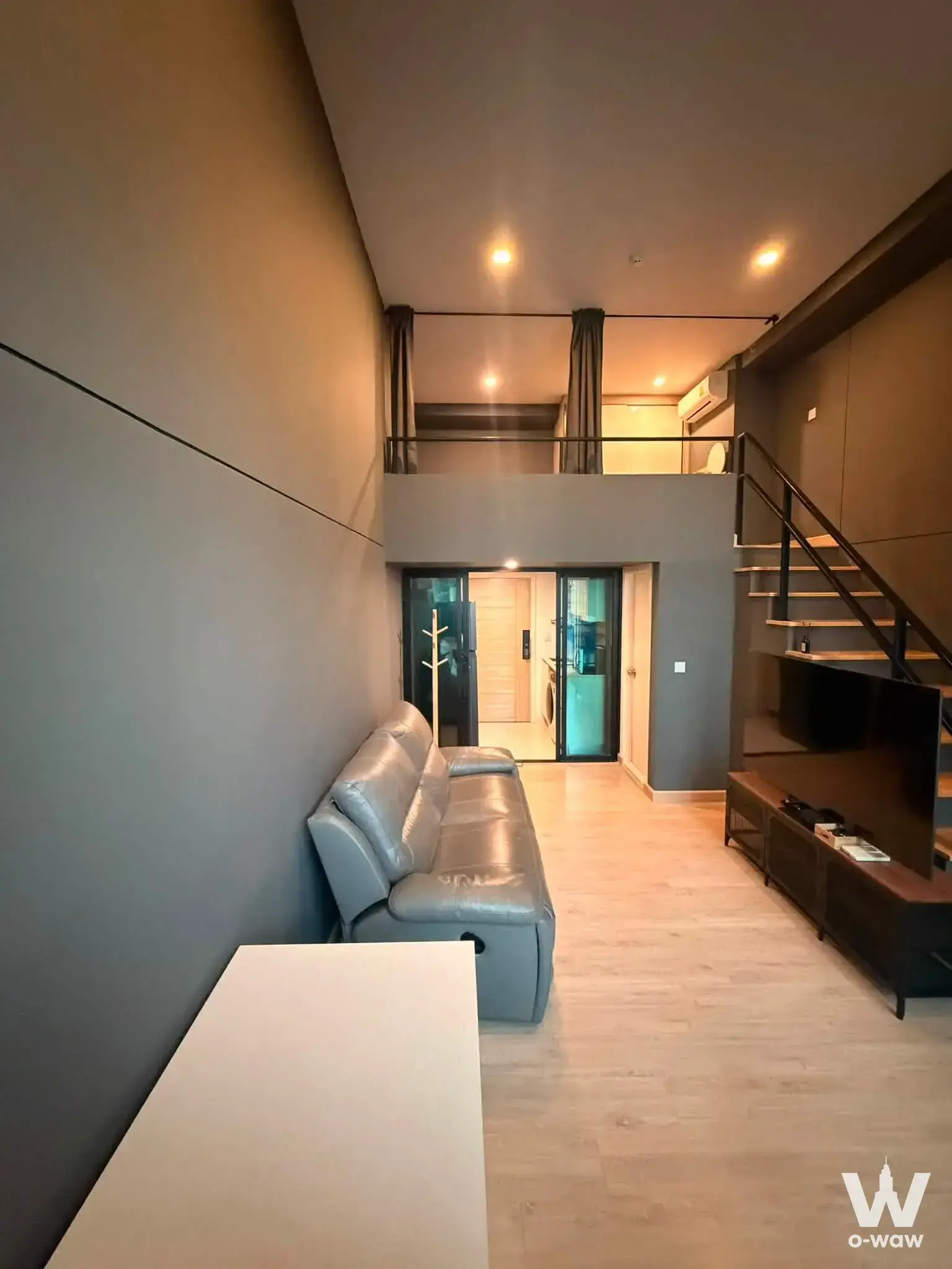 Loft-style living room in Knightsbridge Duplex Tiwanon with high ceilings, grey sofa, and open staircase