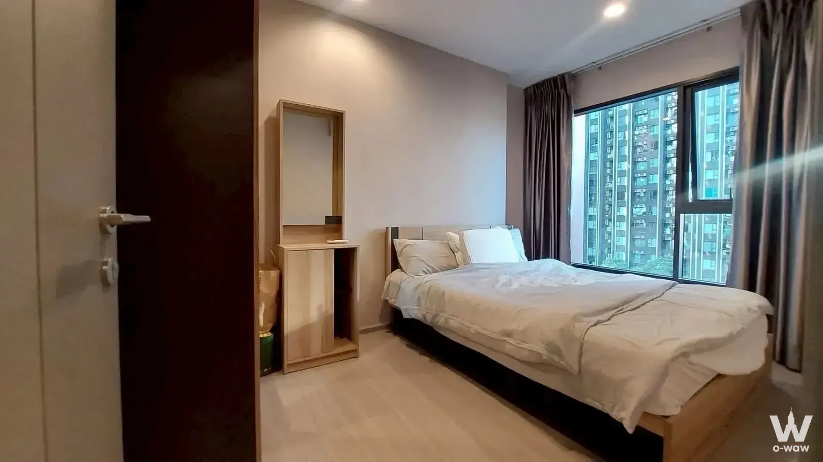 Condo bedroom with queen bed, large window offering high-rise city views, and a tall light-wood vanity unit