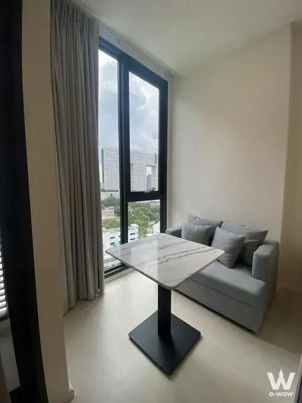 Modern living area in Mazarine Ratchayothin condo featuring grey sofa, marble table, and city view through floor-to-ceiling