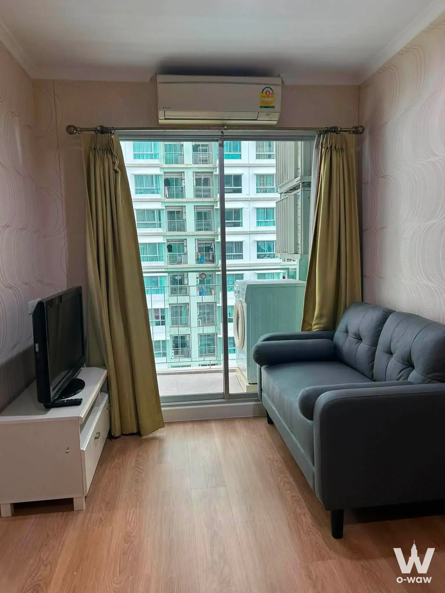 Living room in Lumpini Park Riverside Rama 3 with dark grey leather sofa and sliding glass doors opening to a balcony view
