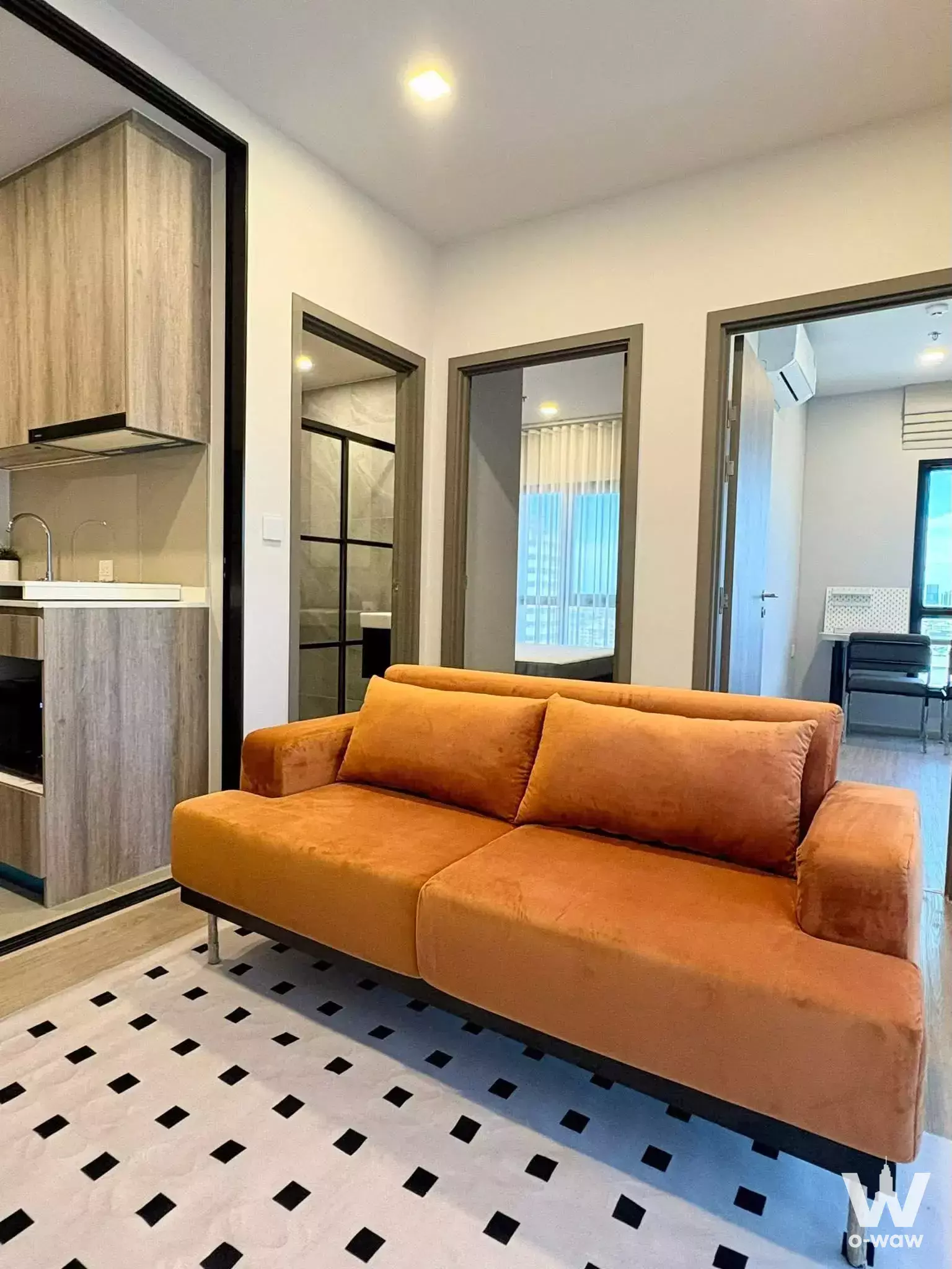 Bright living area in 1-bed condo for rent at M Ladprao featuring burnt-orange sofa and open kitchen