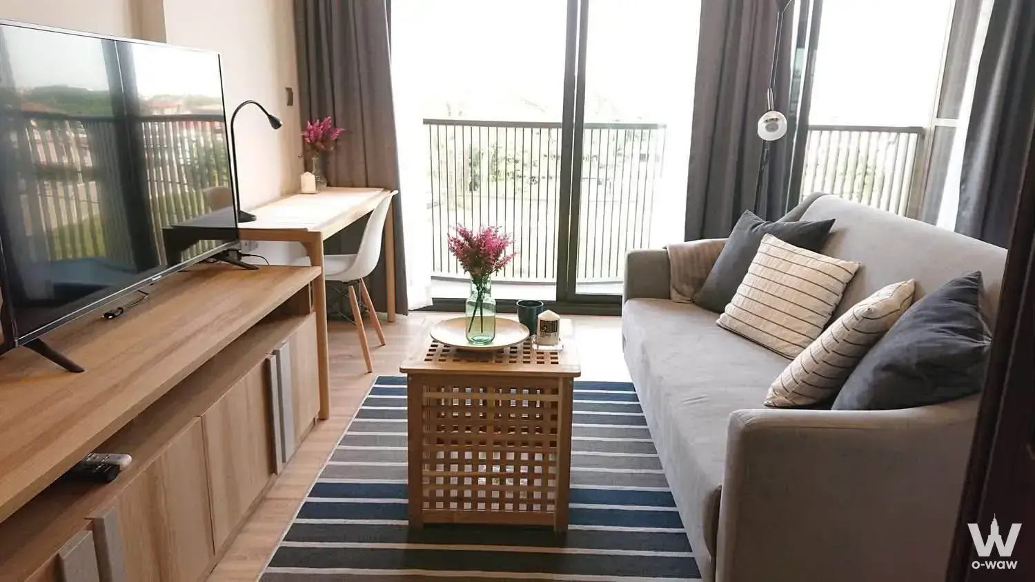 Modern living room with grey sofa, wooden coffee table, and floor-to-ceiling windows overlooking trees