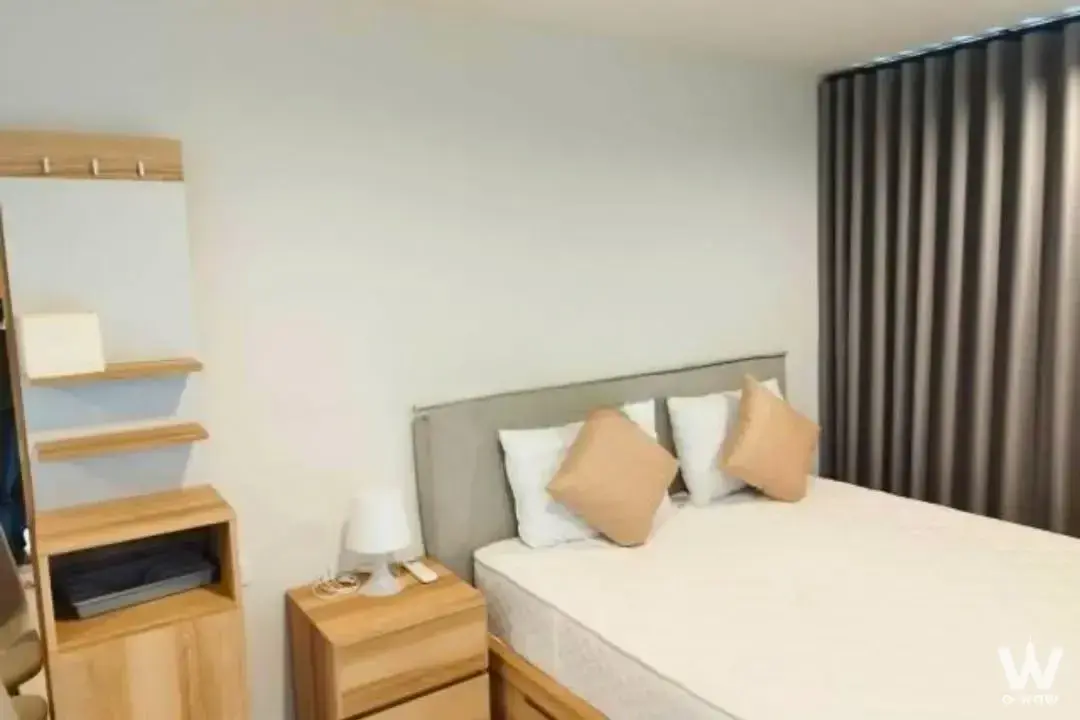 Modern bedroom in 1-bed condo for rent at Ideo Charan 70 featuring grey upholstered bed and light wood accents
