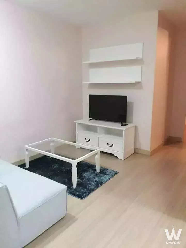 Modern living room with pale pink walls, glass coffee table on blue rug, and white TV console in 2-bed condo for rent at The