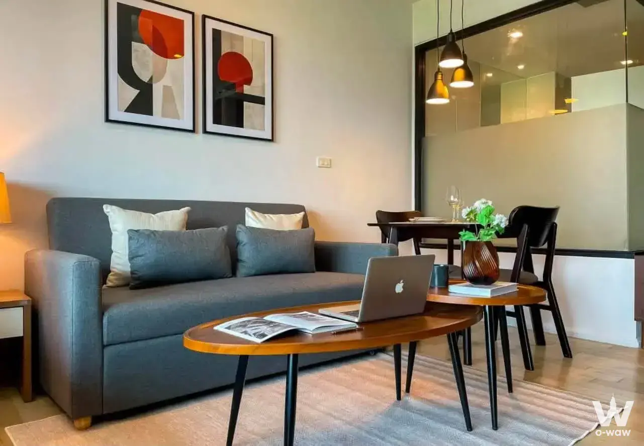Modern living room with grey sofa, wood floors, and dining area in 1-bed condo for rent at Noble Solo Bangkok