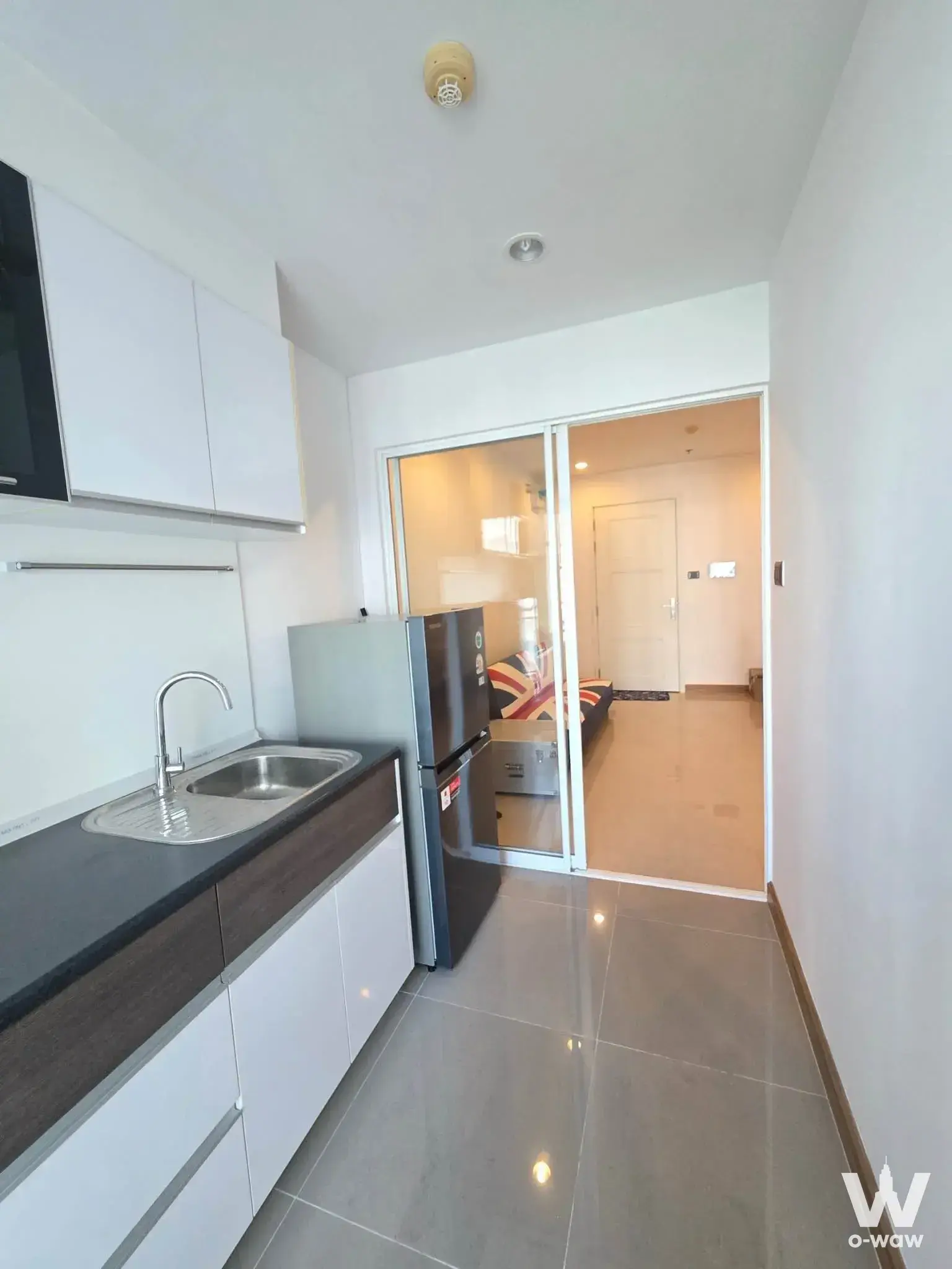 Modern kitchenette with glossy grey tiles and matte black counter in 1-bed condo for sale in Supalai Wellington II