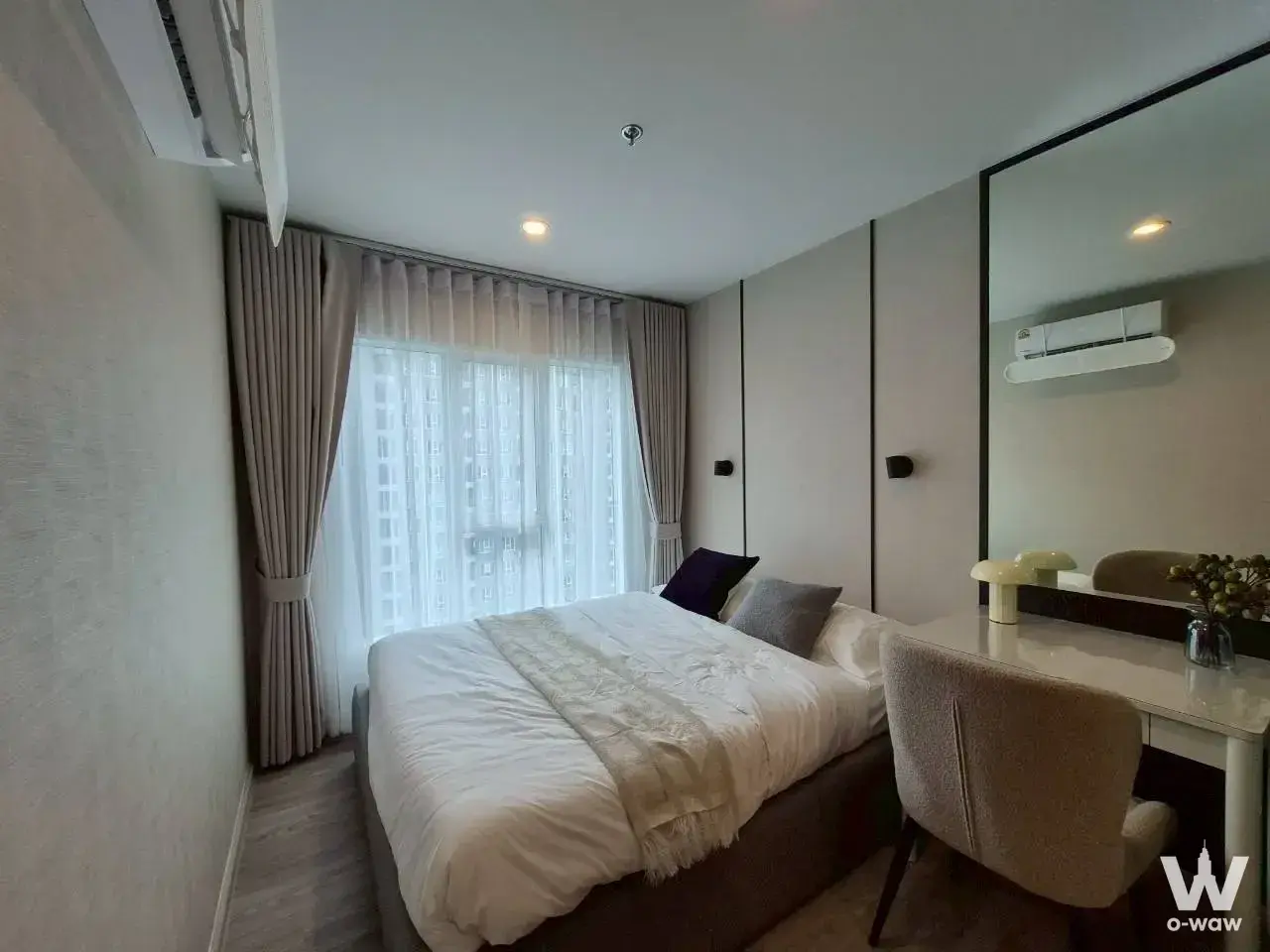Bright bedroom with queen bed, beige curtains, and floor-to-ceiling window city view