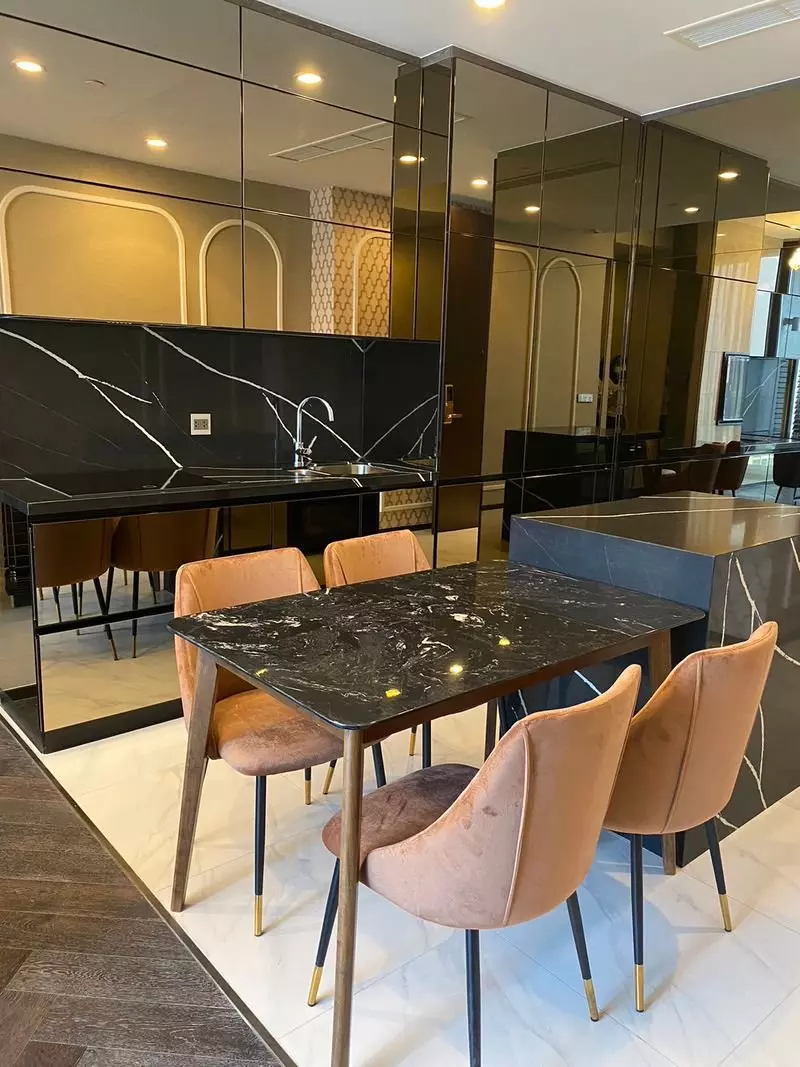Modern dining area with black marble table, peach velvet chairs, and sleek kitchenette in 2-bed condo for rent at THE ESSE