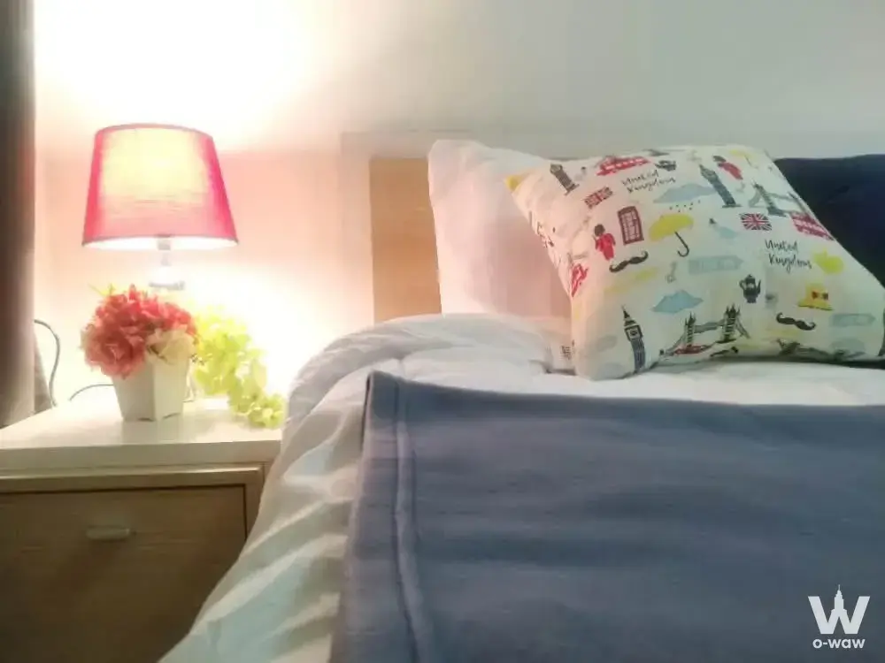 Bedroom in 1-bed May Condo rental with white linens, blue throw, UK-themed pillow, pink lamp on nightstand